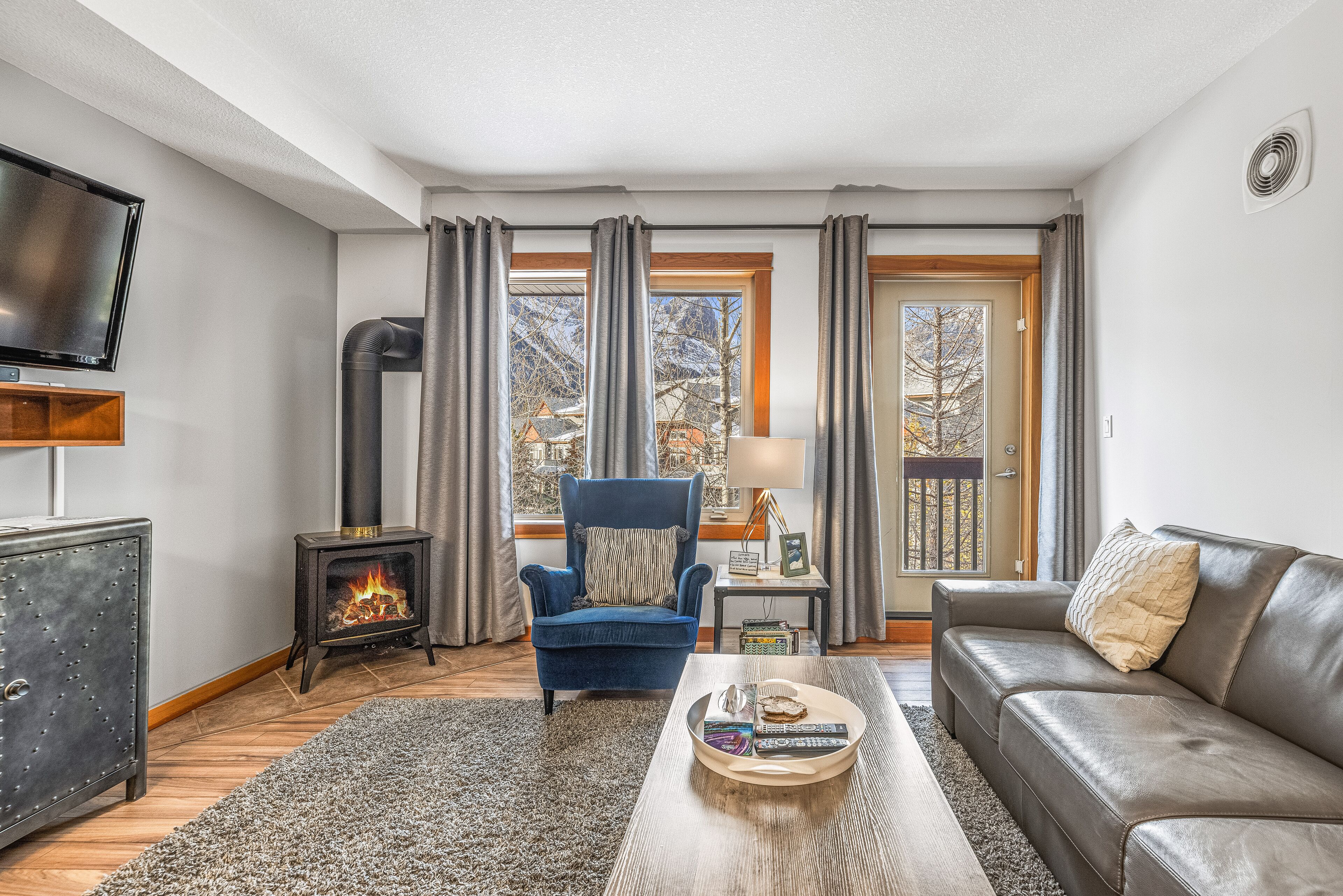 A living room with a fireplace, a sofa, a television, and a view of the outdoors.
