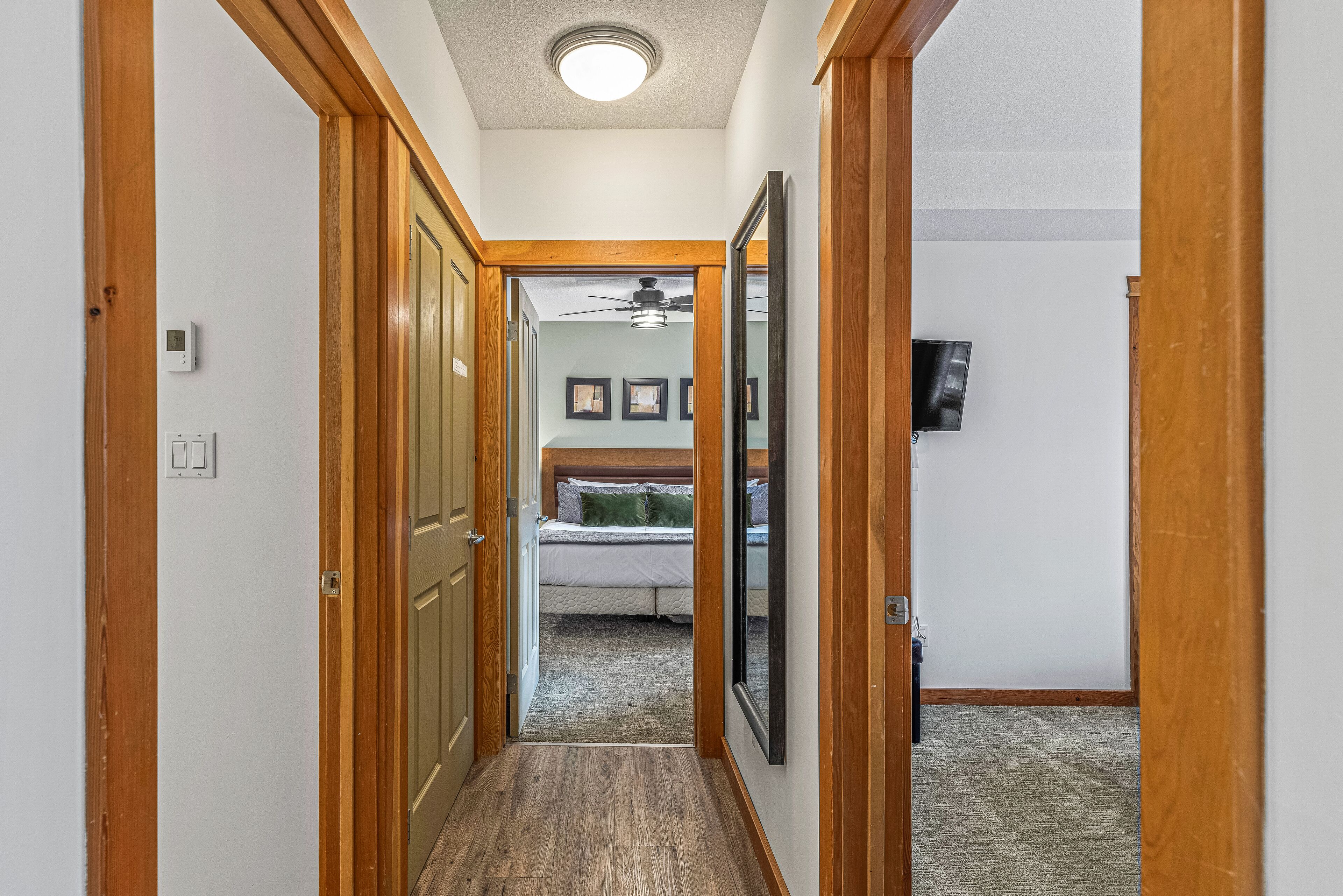 Un couloir avec des portes en bois, un ventilateur de plafond et un lit à l’arrière-plan.