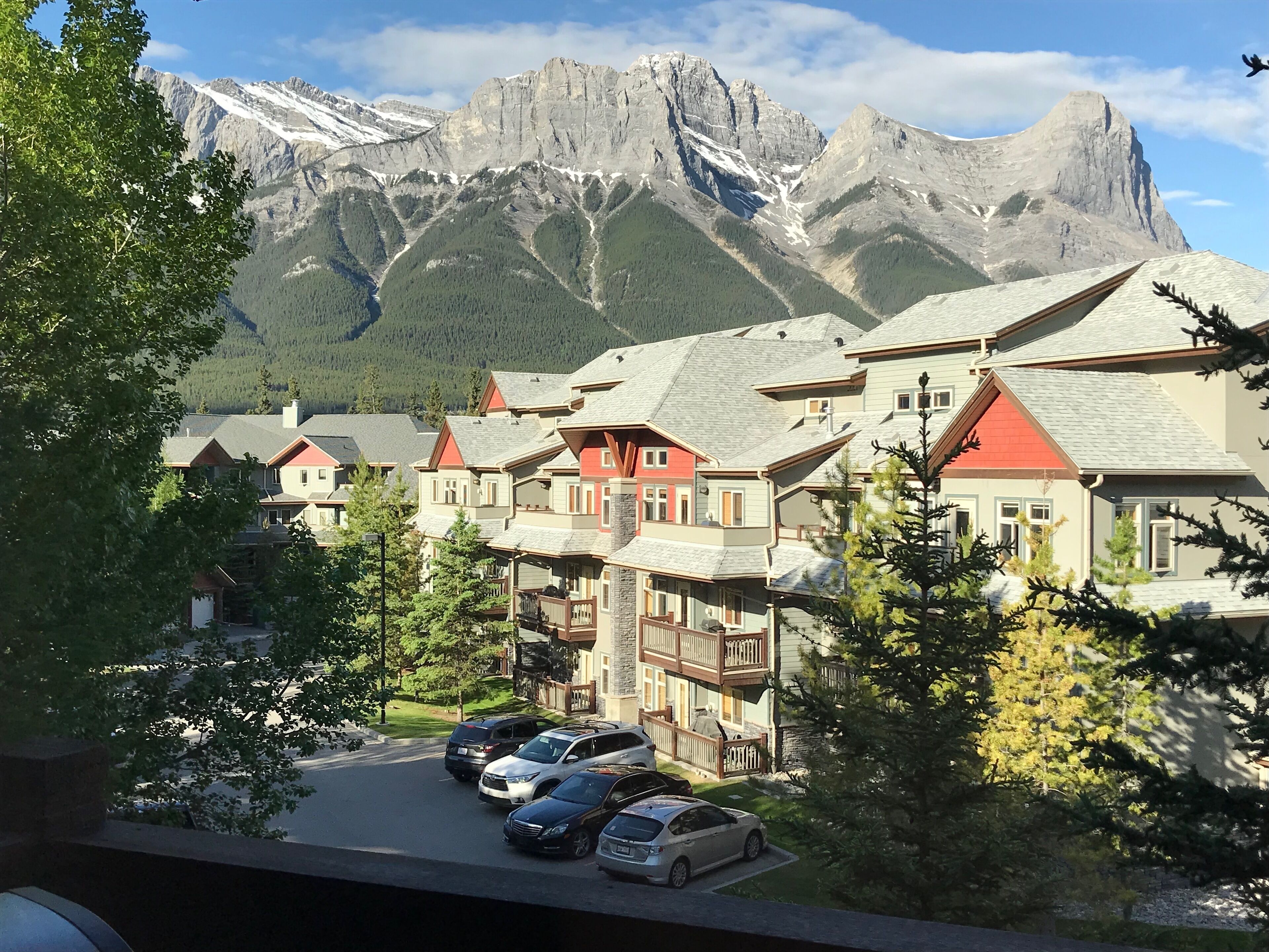 A mountain resort with chalet-style buildings, a parking area, and a view of snow-capped mountains.