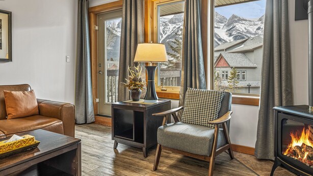 Ein gemütliches Wohnzimmer mit Kamin, einer Couch, einem Sessel und einem Tisch mit Lampe und Pflanze.