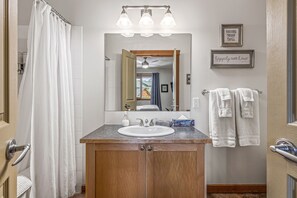 Ein Badezimmer mit einem Holzlaufwerk, einem weißen Waschbecken und einem Spiegel. Handtücher hängen an einem Halter und ein Duschvorhang ist angebracht.