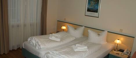 A hotel room with two beds, a nightstand with a lamp, a framed picture on the wall, and a window with curtains.