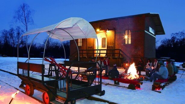 A covered wagon with a canopy, a fire pit, and a brick building in the background. - Land Gut Hotel Weisser Schwan (Zossen)