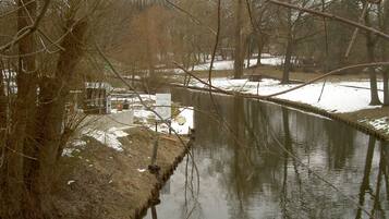 A calm river with bare trees and snow patches on the banks, reflecting the sky.
