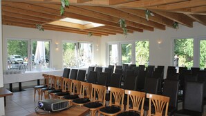 A conference room with rows of chairs, a projector, and large windows offering a view of the outdoors. - Land Gut Hotel Weisser Schwan (Zossen)