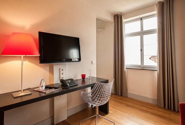 A hotel room with a flat-screen TV, a desk with a telephone, a chair, and a window with curtains. - Villa Behr (Wendlingen am Neckar)