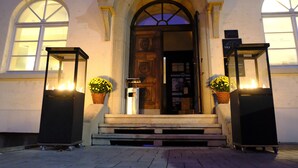 A building entrance with a wooden door, two potted plants, and two standing lanterns. - Villa Behr (Wendlingen am Neckar)