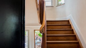 Una escalera de madera con barandilla, que lleva a una habitación con puerta y ventana.