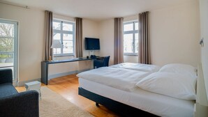 A hotel room with a bed, a desk with a chair, a TV, and two windows with curtains. - Villa Behr (Wendlingen am Neckar)