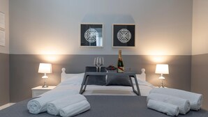 A hotel room with a bed, two bedside tables, a nightstand, a wall-mounted lamp, a framed picture, and a bottle of champagne. - Casa Solmes Rooms (Olbia)