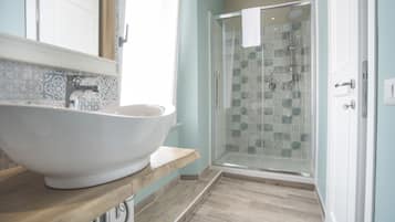 A bathroom with a large white vessel sink, a glass-enclosed shower, and patterned tiles on the walls.