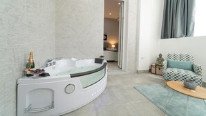 A modern bathroom with a freestanding bathtub, a small table with a bottle and fruit, and a patterned armchair. - Casa Solmes Rooms (Olbia)
