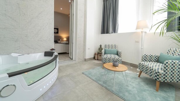 A modern living room with a jacuzzi, patterned furniture, and a view of the adjacent kitchen. - Casa Solmes Rooms (Olbia)