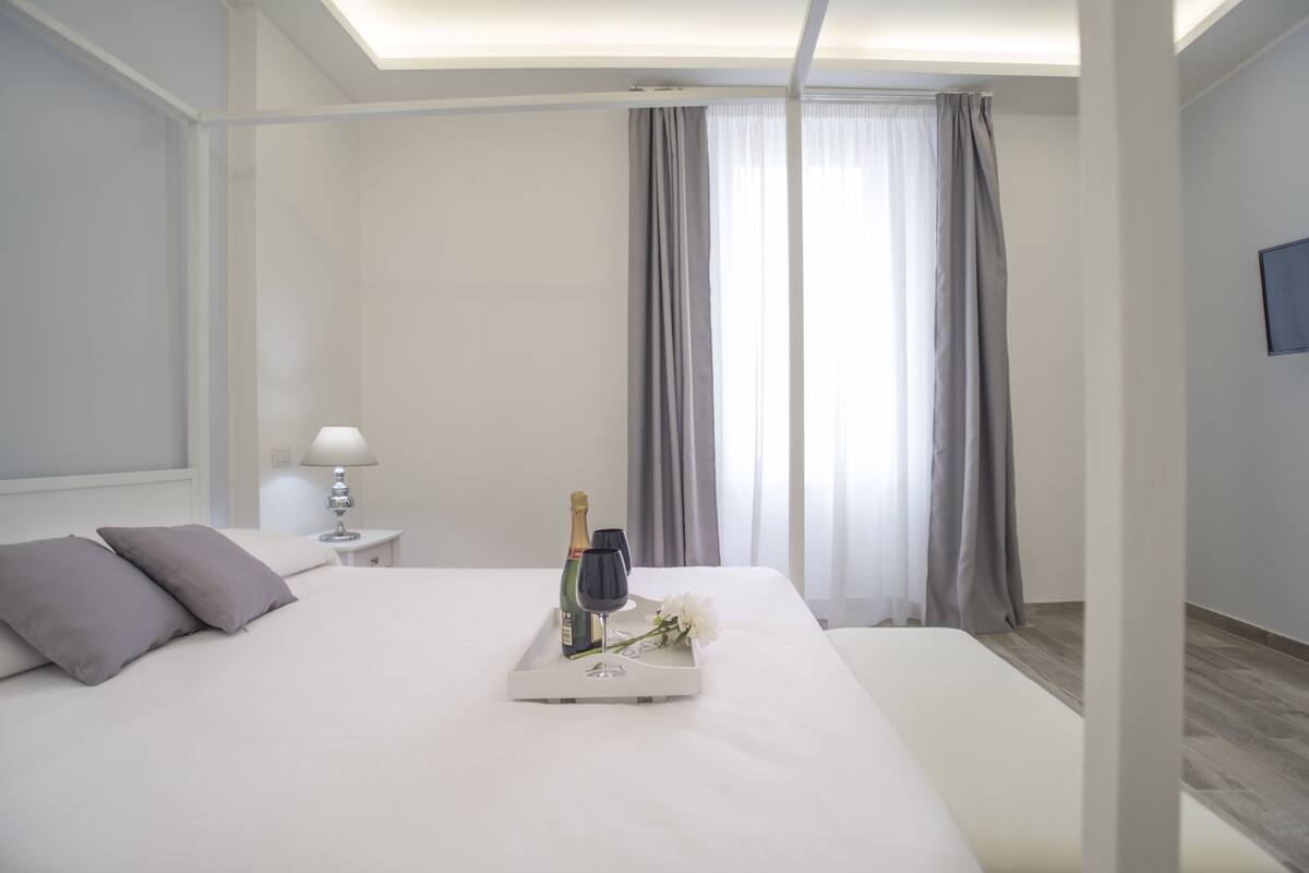 A neatly made bed with a tray containing a bottle, a glass, and a flower.
