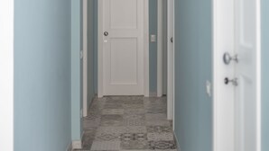 A narrow hallway with light blue walls and patterned gray and white tiles. - Casa Solmes Rooms (Olbia)