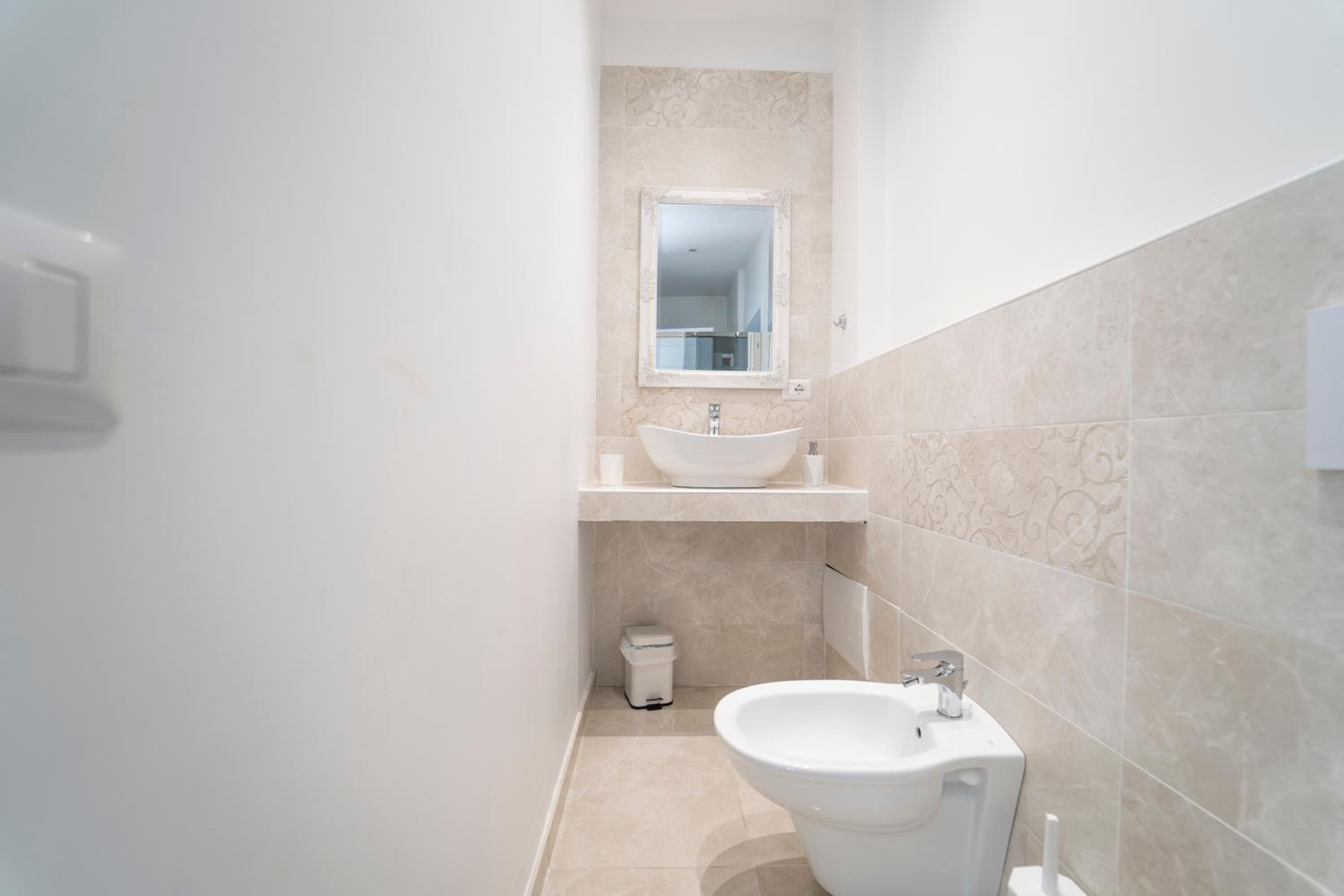 A modern bathroom with a white sink, a mirror, and a bidet.