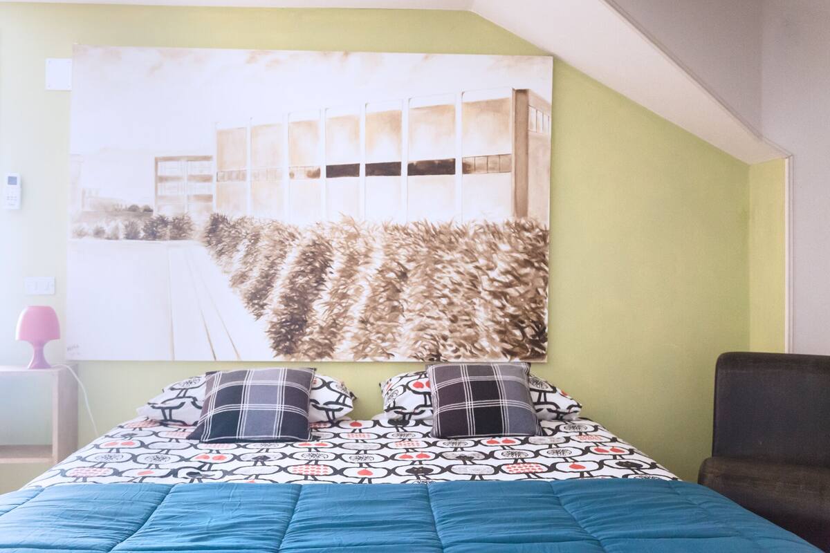 Une chambre à coucher avec un lit, des oreillers et un grand tableau abstrait accroché au mur.