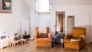 Un salón acogedor con dos sillones color mostaza, una mesa de centro de madera, un radiador y una ventana con luz natural.