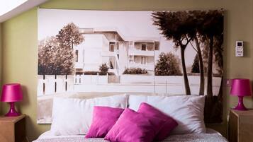 Una camera da letto con un letto, due lampade rosa e un grande quadro raffigurante un edificio e alberi.