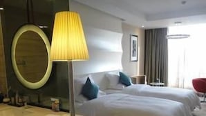 Et hotelværelse med et rundt spejl, en sengetablelampe, to senge med puder, et lille bord og en rød stol.