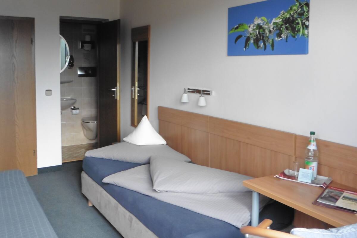 A hotel room with a bed, a desk, a chair, a bathroom, and a painting on the wall.