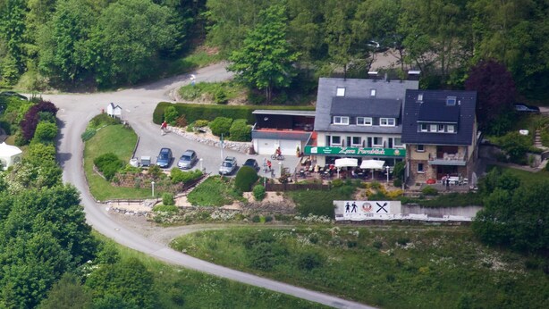 An aerial view of a building with a restaurant named "Zara Foodhall" on the ground floor, surrounded by greenery and a parking area. - Pension zum Fernblick (Willingen)