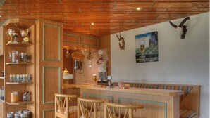 A wooden bar area with bar stools, shelves with glassware, and a poster on the wall. - Pension zum Fernblick (Willingen)