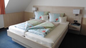 A neatly made bed with floral bedding, two bedside tables with lamps, and a wooden headboard. - Pension zum Fernblick (Willingen)