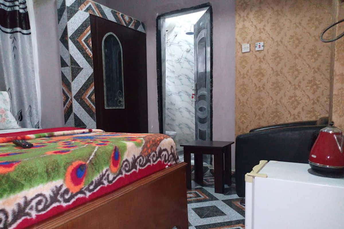 A bedroom with a bed, a dresser, a mirror, and a red kettle on a table.
