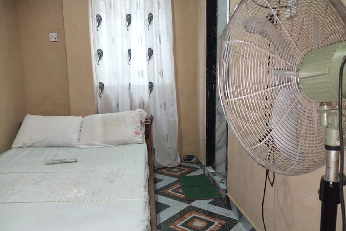 A bedroom with a bed, a fan, a patterned curtain, and a geometric patterned floor.