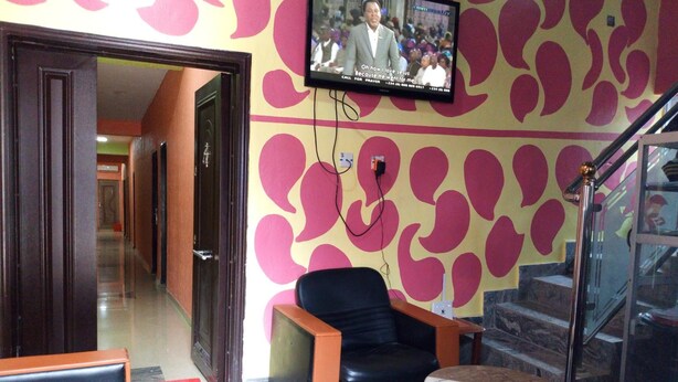 Un hall con una televisión montada en la pared, un sillón de cuero negro, una mesita redonda y una escalera.