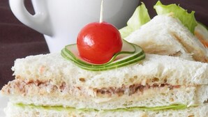 Un sándwich con cereza encima, lechuga y una taza al fondo.