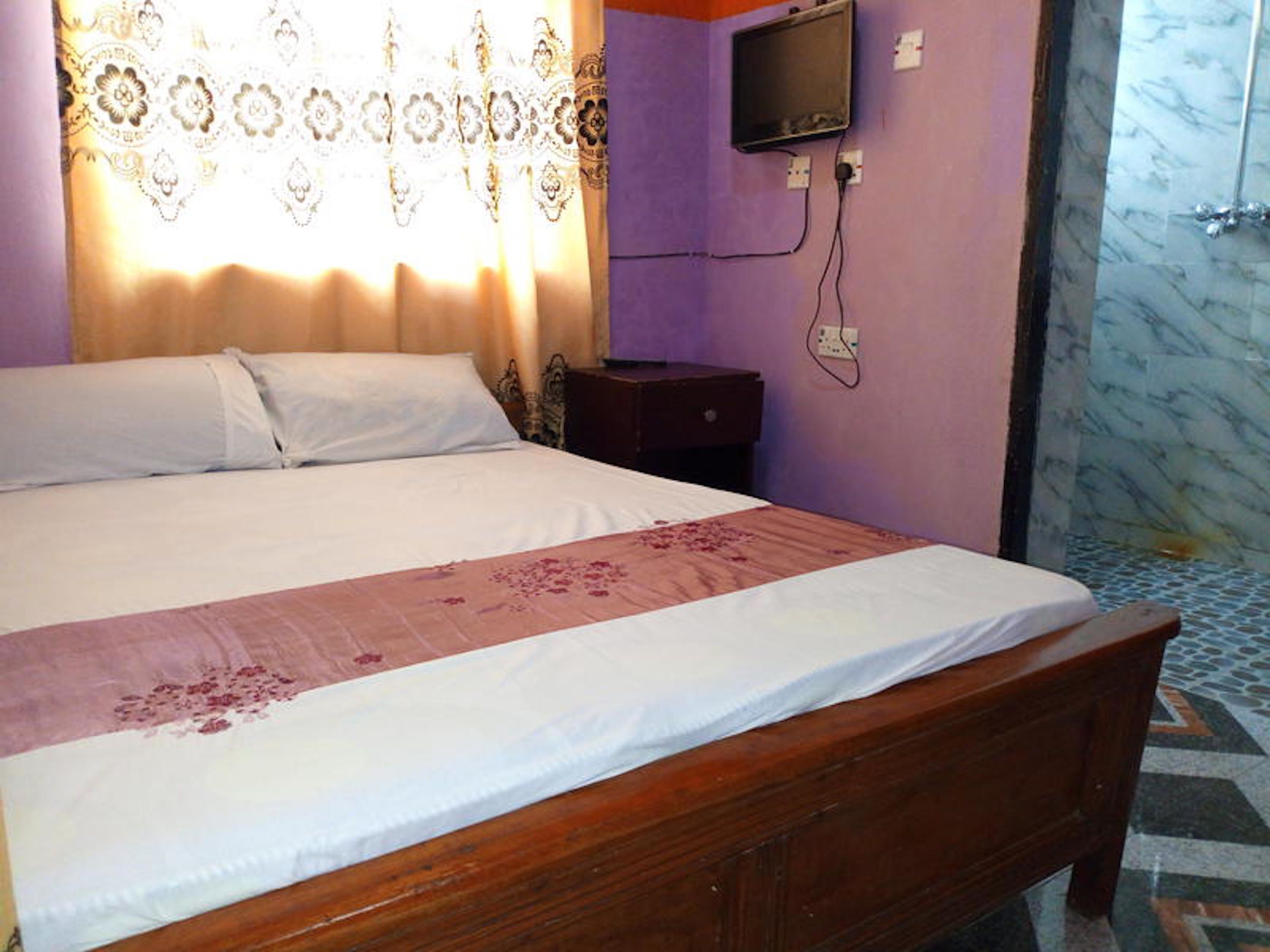 A bedroom with a wooden bed, a nightstand, a television mounted on the wall, and patterned curtains.