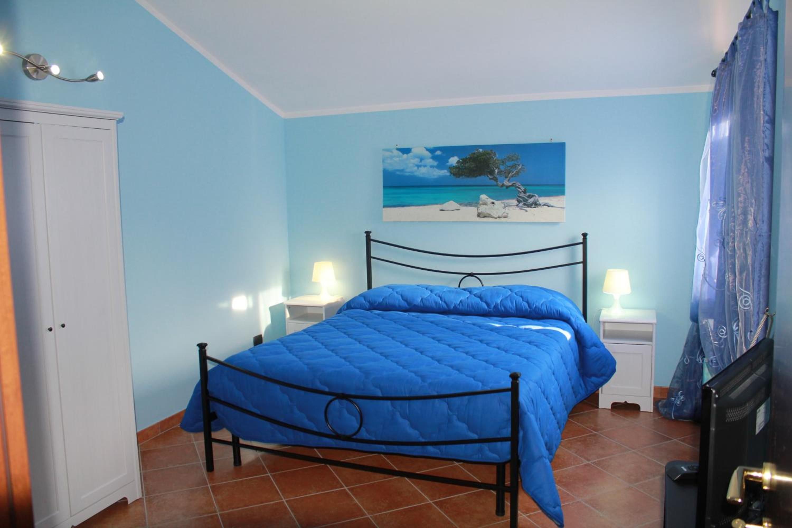 Un dormitorio con una cama, dos mesitas de noche, una lámpara de noche, un cuadro y una puerta.