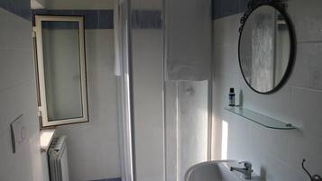 A bathroom with a shower, a sink, a mirror, and a radiator.