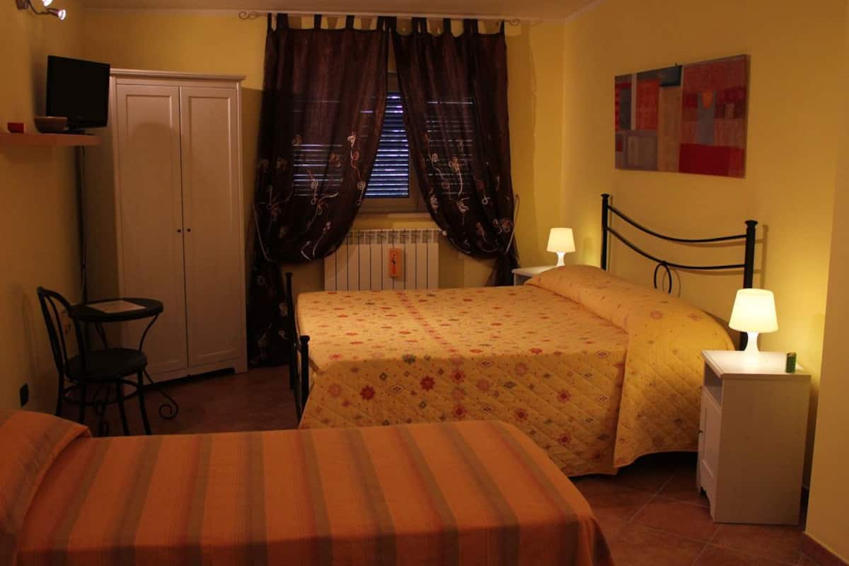 Un dormitorio con dos camas, un escritorio, una silla, un radiador y un televisor en una estantería.