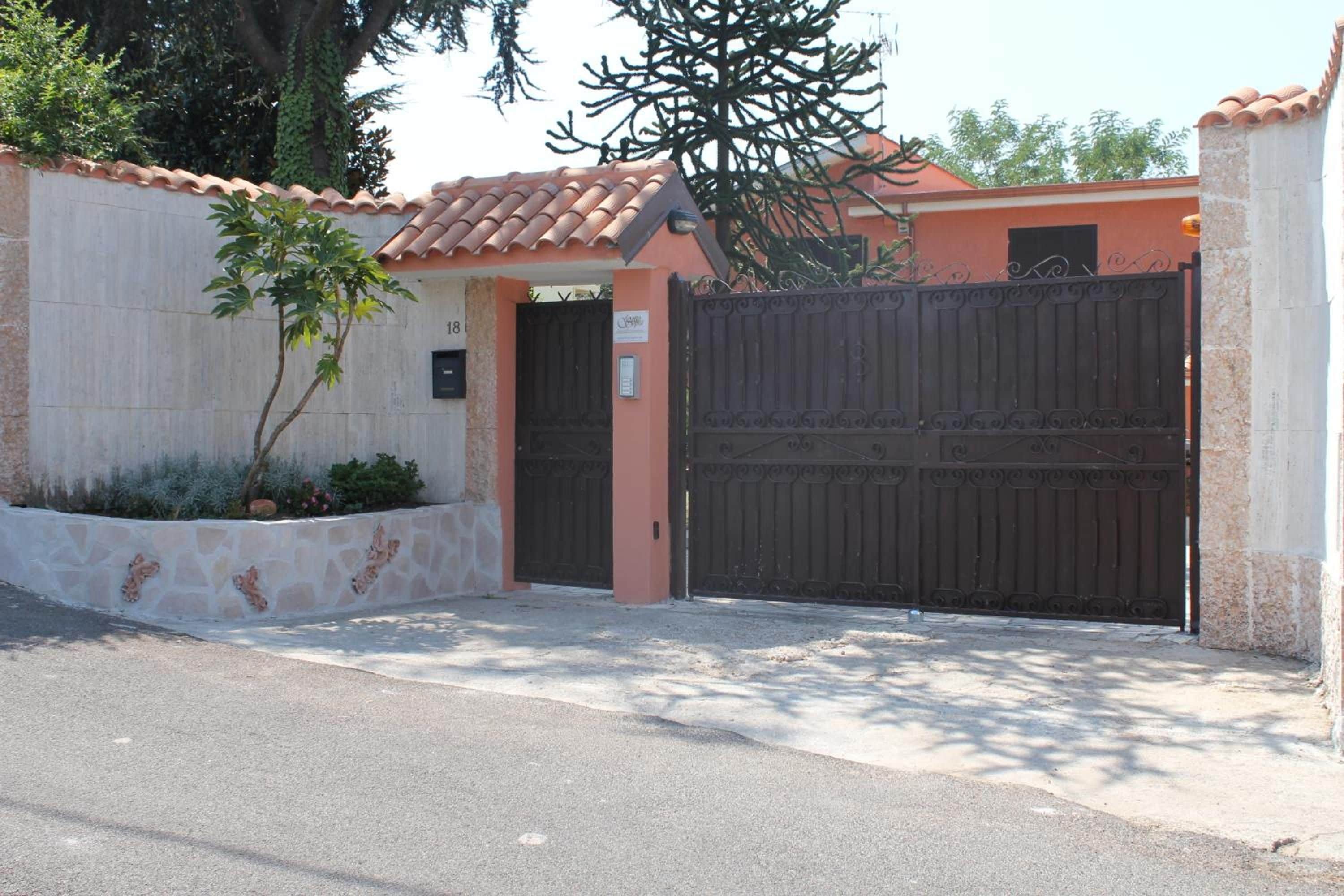 A gated entrance with a metal gate, a stone wall, and a small tree.