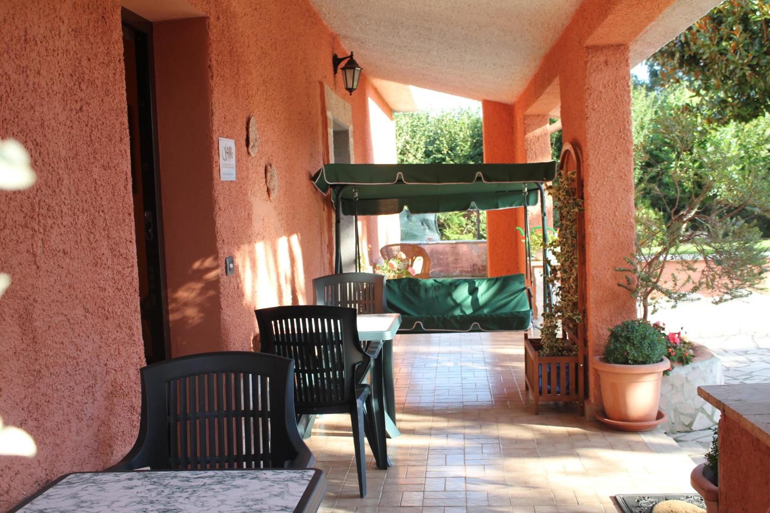 Un patio al aire libre con una mesa, sillas, un toldo verde y plantas en macetas.