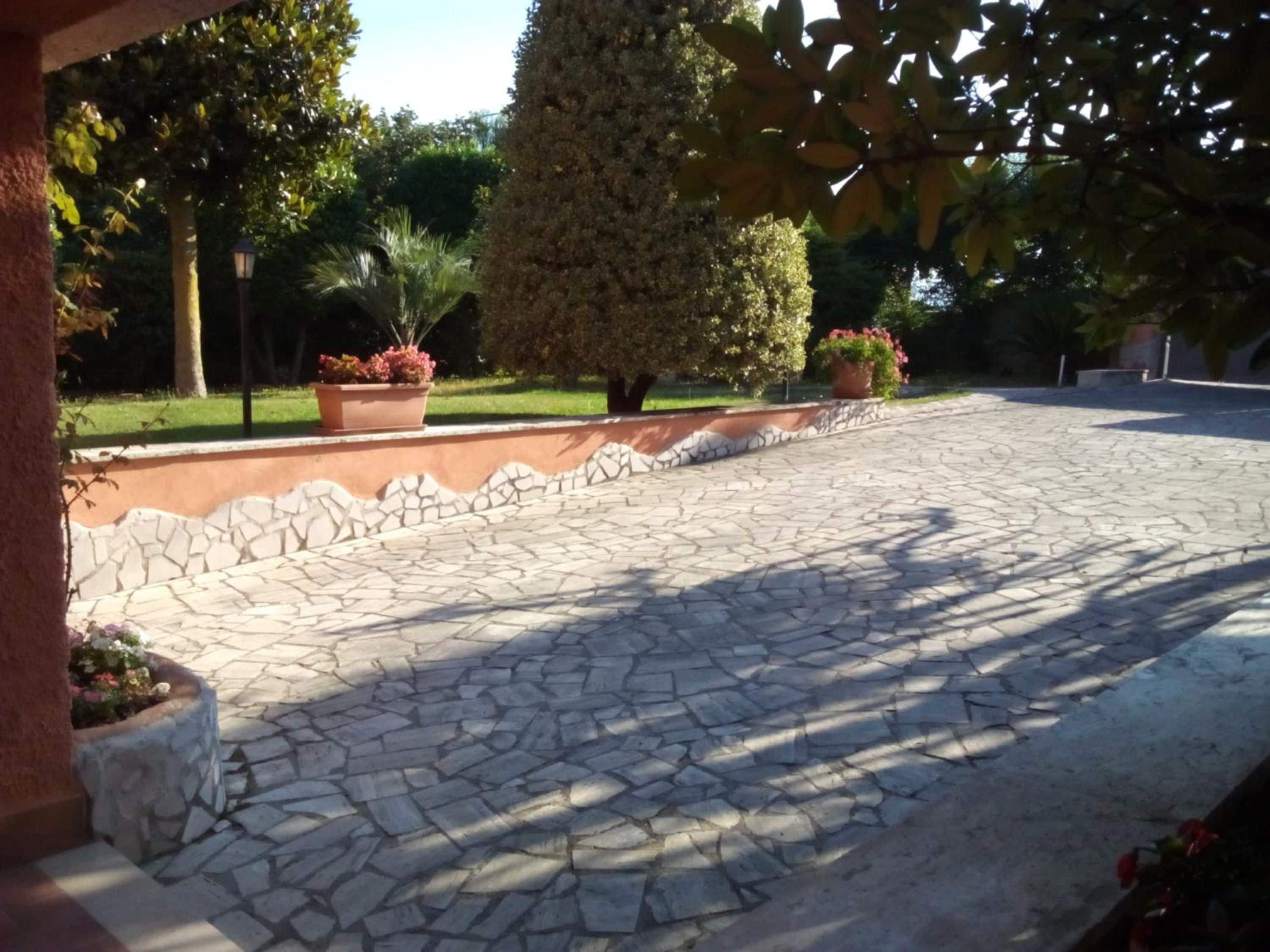 A paved courtyard with stone tiles, surrounded by a low stone wall and potted plants.