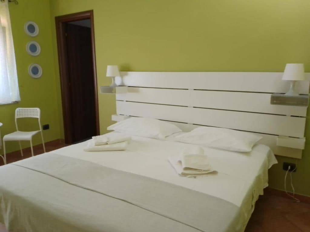 Una habitación de hotel con una cama, dos lámparas de noche, una silla y una puerta.