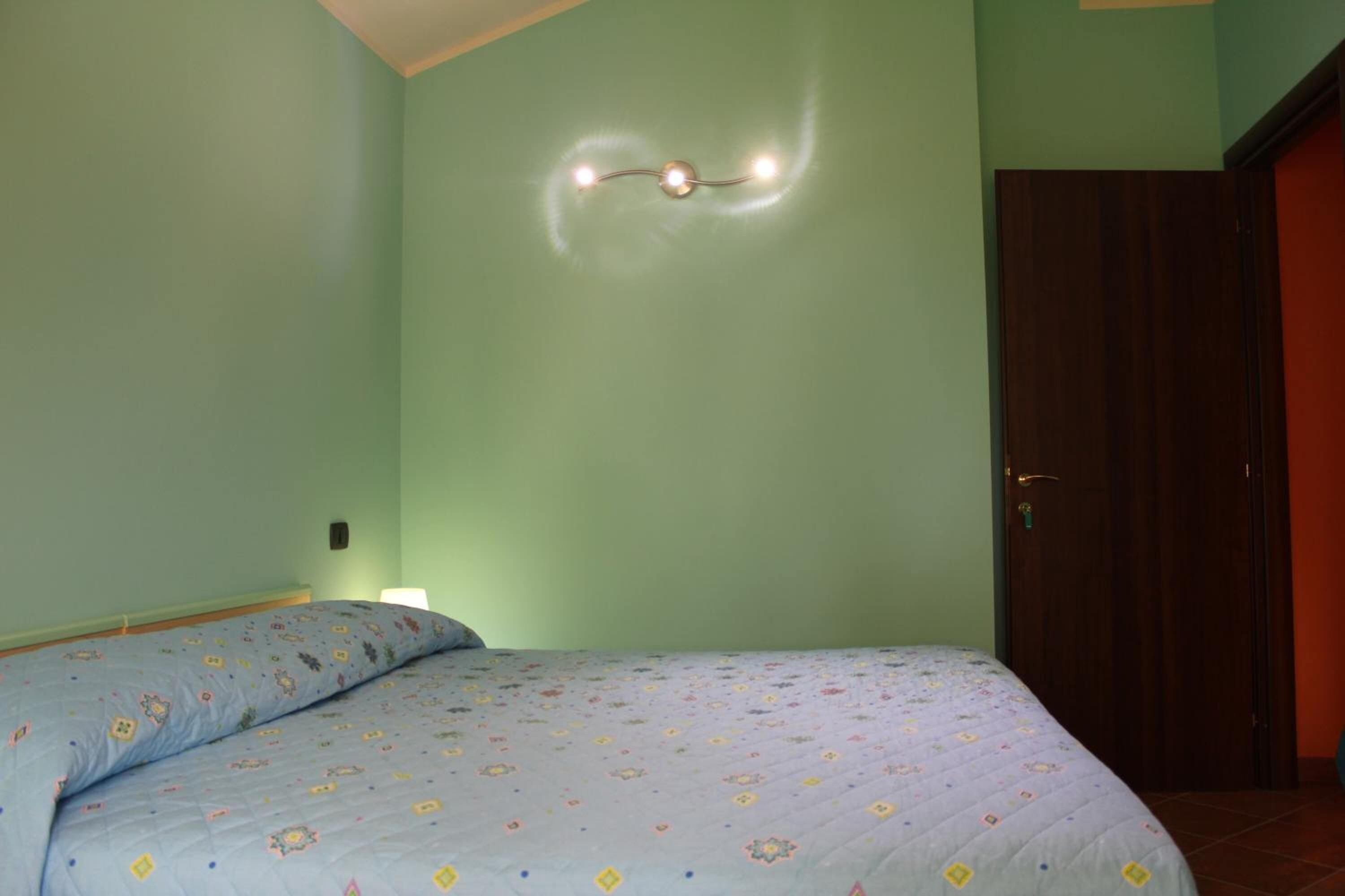 Una habitación con una cama, un accesorio de luz en la pared y una puerta.