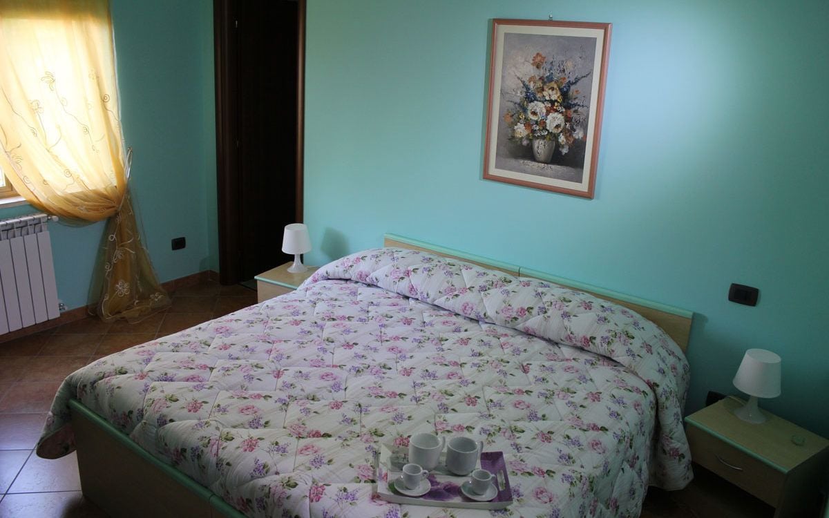 Une chambre à coucher avec une couvre-lit à motifs floraux, une table de chevet avec une lampe et un tableau floral encadré accroché au mur.