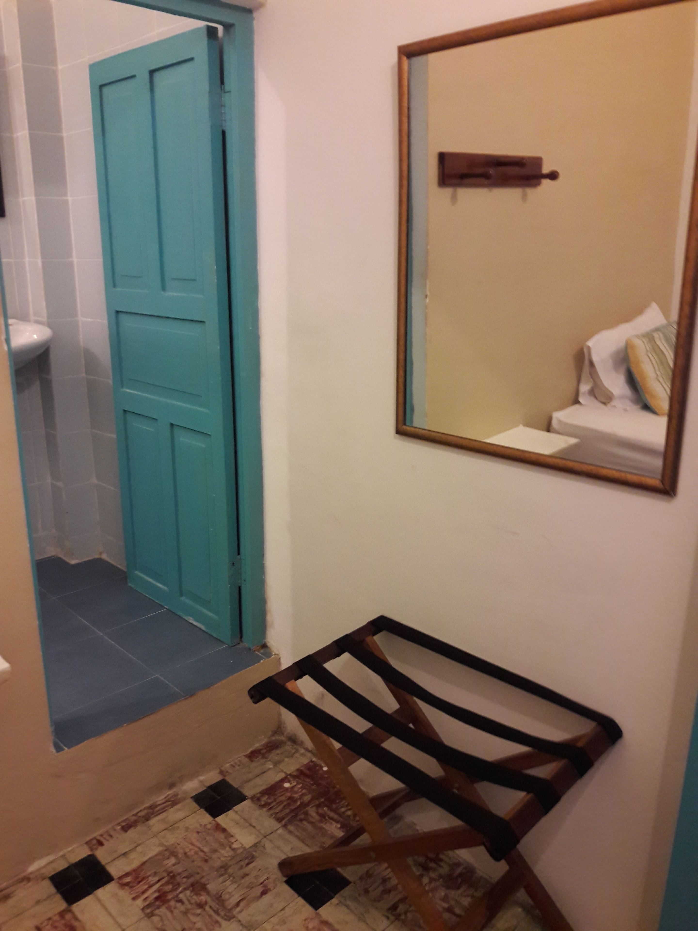 Ein Badezimmer mit einer türkisblauen Tür, einem Spiegel und einem Holzbstuhl.