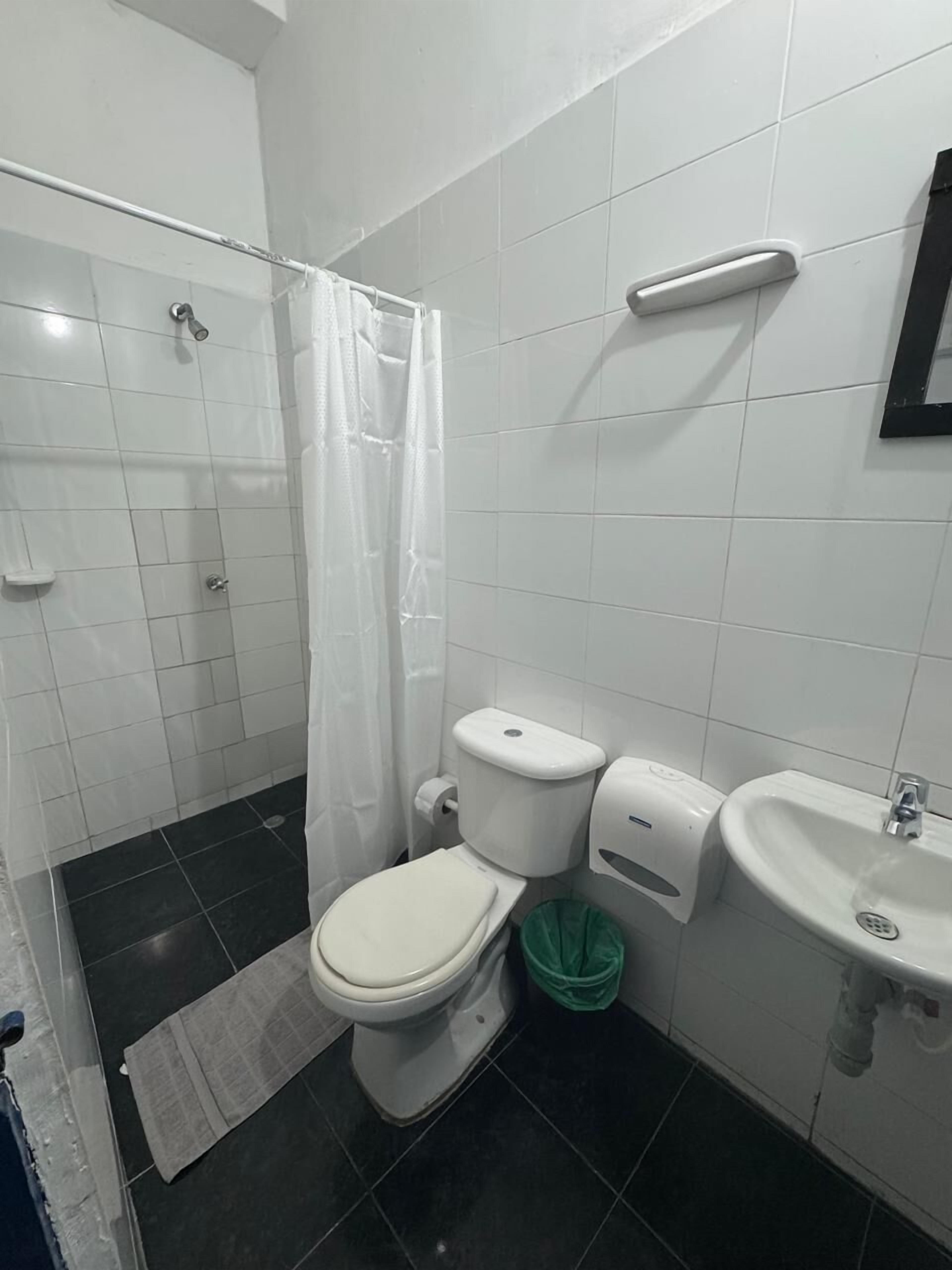 A bathroom with a toilet, a sink, a shower, and a green trash bin.