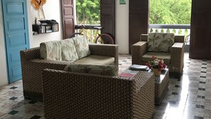 A room with a wicker sofa, a blue door, a bookshelf, and a view of greenery outside. - Casa 1811 (Cartagena)