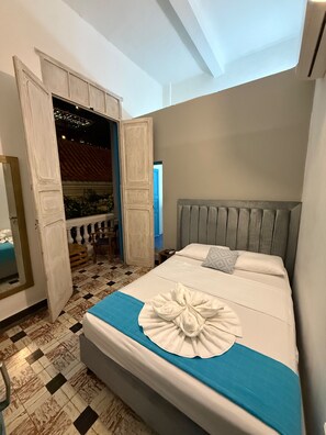 A hotel room with a bed, a blue towel, a wooden door, and a checkered floor. - Casa 1811 (Cartagena)