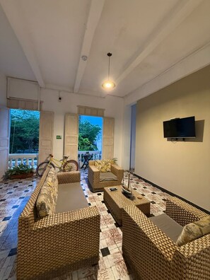 A room with wicker furniture, a flat-screen TV, and a view of greenery outside. - Casa 1811 (Cartagena)