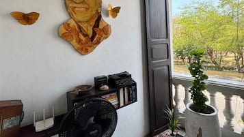 A room with a large window, a potted plant, a bookshelf, and a wall-mounted fan.