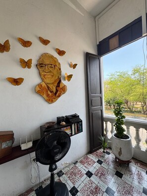 A room with a large window, a potted plant, a bookshelf, and a wall-mounted fan. - Casa 1811 (Cartagena)