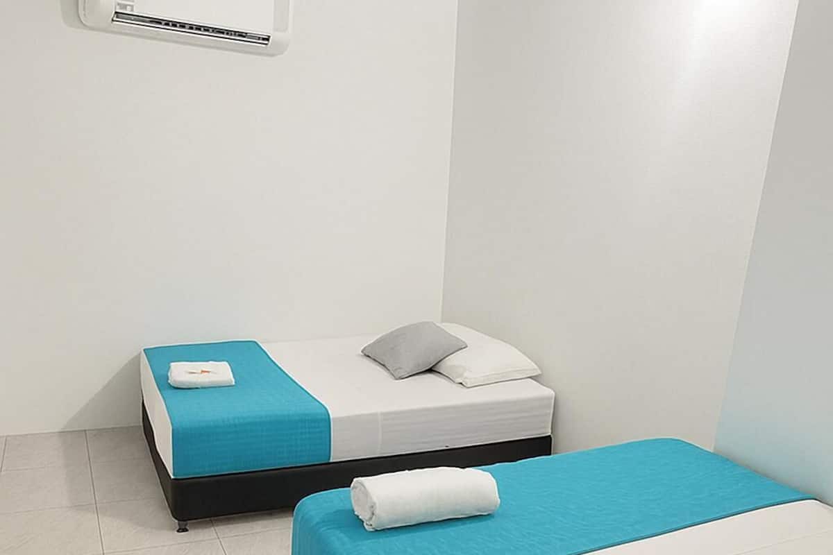 Quarto de hotel com duas camas, cada uma com colcha azul e almofadas brancas.